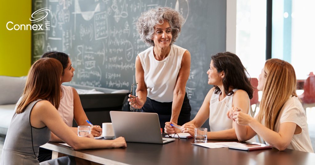 Boss speaks to employees at a desk in an office about team productivity
